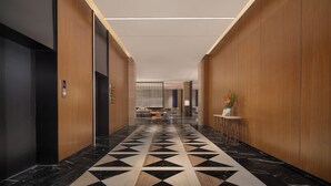 A modern hotel lobby with a geometric patterned floor, wooden paneling, and a reception area with a small table and chairs. - Wanda Moments Alar (Aral City)