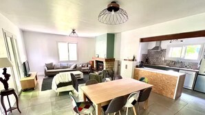 A spacious living area with a wooden dining table, a sofa, and a kitchen area with a tiled backsplash. - Green cocoon with private swimming pool (Cunèges)