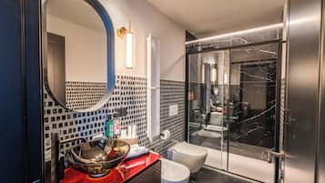 Une salle de bain moderne avec une douche à parois de verre, un miroir rond et un plan de toilette rouge.