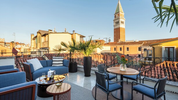 A rooftop terrace with outdoor seating, a view of a tower, and a palm tree. - Palazzo Rota Luxury Apartments (Venice)