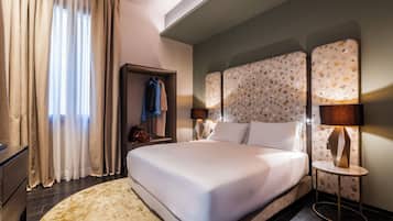 A hotel room with a large bed, a bedside table with a lamp, a wardrobe, and a window with curtains.