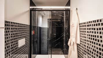 A modern bathroom with a glass shower enclosure, a white sink, and a towel hanging on the wall.