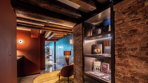 A modern interior with exposed brick walls, a wooden ceiling, and a well-lit reading area with a bookshelf. - Palazzo Rota Luxury Apartments (Venice)