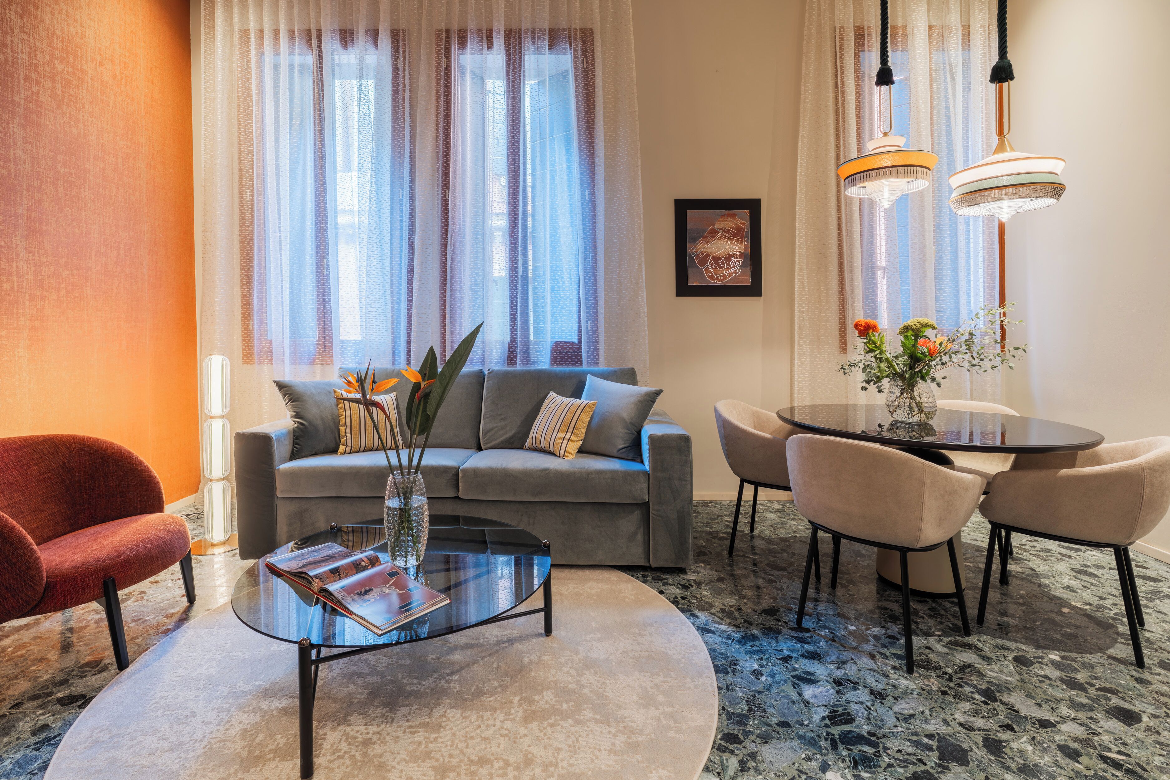 A modern living room with a grey sofa, a glass coffee table, and a dining area with a round table and chairs.