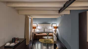 Une chambre d’hôtel avec un lit, des lampes de chevet, une machine à café, un plateau avec des tasses et des en-cas, et une petite table ronde sur laquelle est posé un vase.