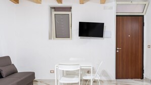 Une pièce comprenant un canapé, un téléviseur fixé au mur, une porte en bois et une fenêtre avec un store.