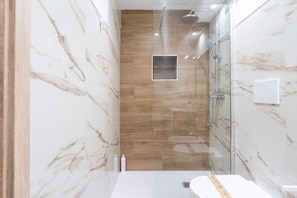A modern bathroom with a glass shower enclosure, a wooden floor, and a white sink.