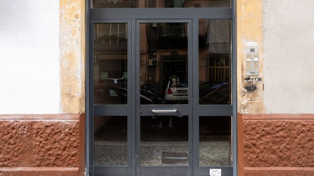 Une entrée d’immeuble avec une porte en verre, une poignée en métal et un petit panneau au sol.