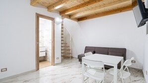 Une pièce moderne avec un sol en marbre blanc, un plafond en bois, un canapé gris et une table blanche avec des chaises.
