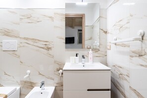 A modern bathroom with marble walls, a white sink, and a mirror.