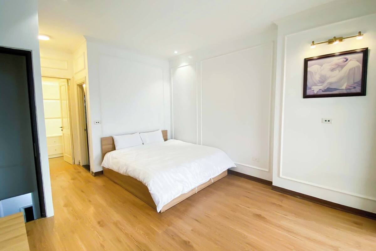 A bedroom with a wooden floor, a bed with white bedding, a door leading to a closet, and a painting on the wall.