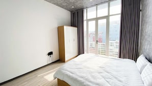A bedroom with a large bed, a wardrobe, a radiator, and a window with curtains. - Eco Nest Apartment & Stay (Hanoi)