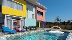 Een kleurrijk gebouw met een zwembadgedeelte, compleet met ligbedden en een opblaasbaar vlot in de kleuren van de regenboog.