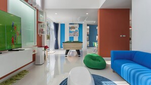 Een moderne woonkamer met een flatscreen televisie, een pooltafel, een groene relaxfauteuil en een blauwe bank.