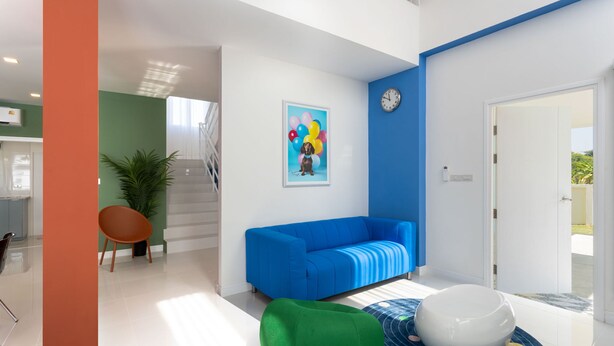 A modern living room with a blue sofa, a green bean bag, and a white spherical chair. A colorful painting of a dog with balloons is on the wall.