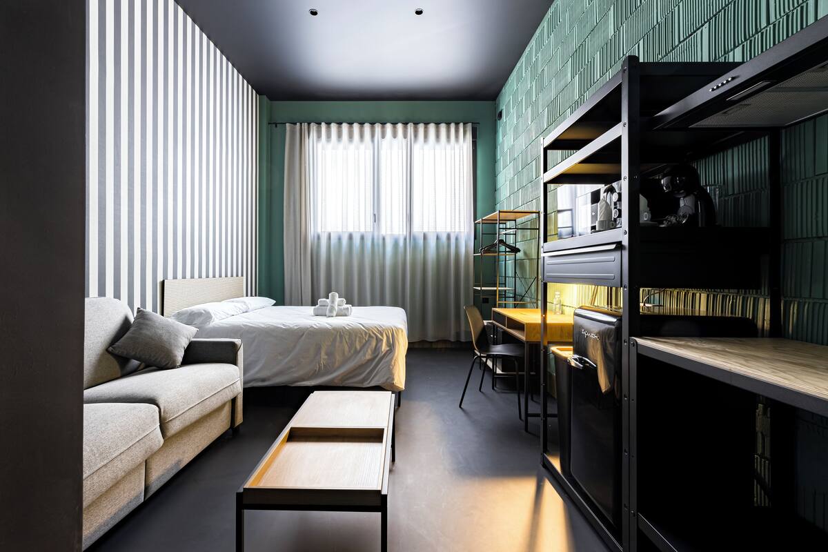 A modern hotel room with a bed, sofa, desk, and built-in wardrobe.