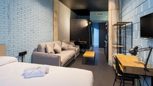 A modern hotel room with a brick wall, a sofa, a bed, a desk, and a chair. - Apartamentos HEY U (Murcia)