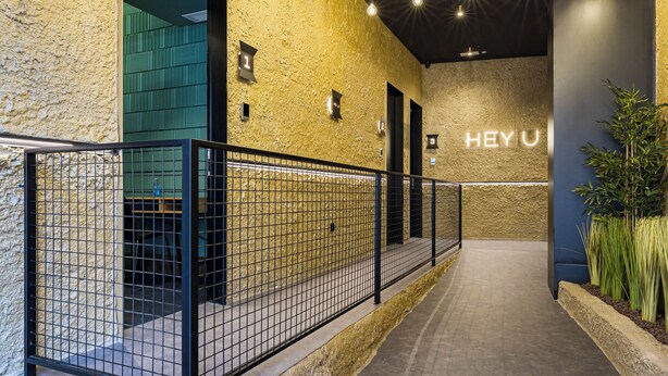 A hallway with a textured wall, a metal railing, and a 'HEY U' sign on the wall. - Apartamentos HEY U (Murcia)