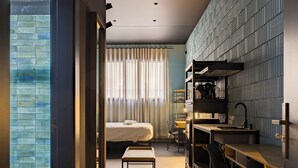 A modern hotel room with a bed, a small table, a desk, and a kitchenette. - Apartamentos HEY U (Murcia)