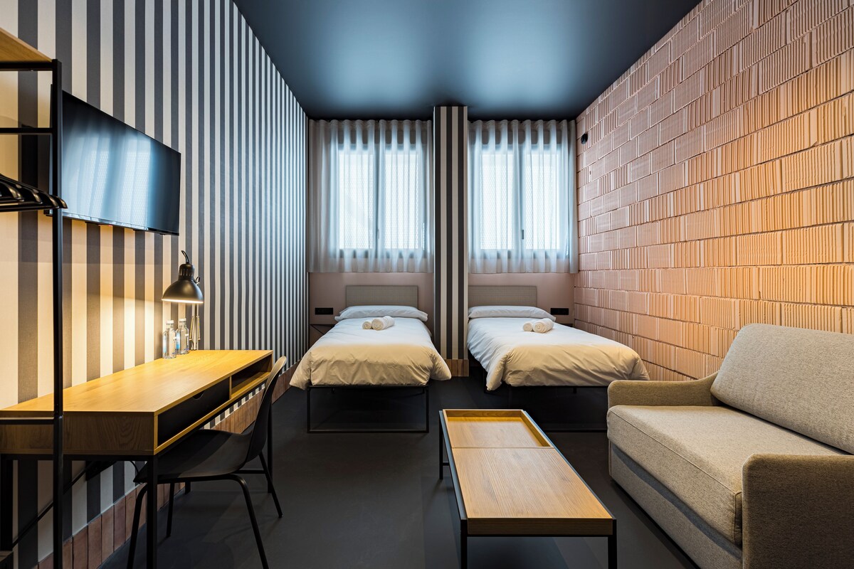 Una habitación de hotel moderna con dos camas, un sofá, un escritorio y un televisor.