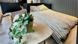 A bedroom with a bed, a small table with a plant, and a view of a kitchen and living area. - ConfortDream your haven of peace in Mulhouse (Mulhouse)