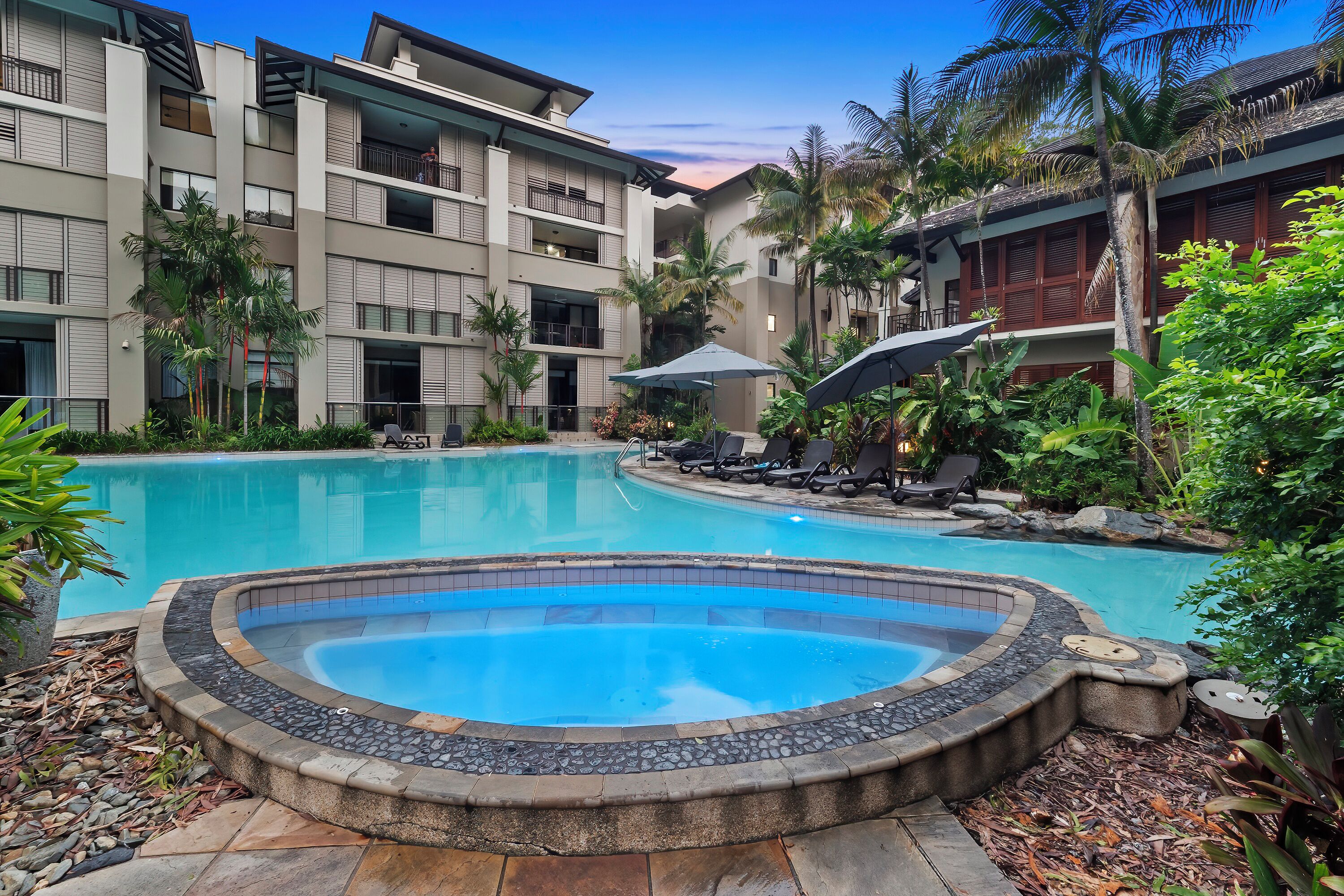 Un hôtel doté d’une piscine, entourée d’une végétation luxuriante et de palmiers.