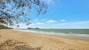 A sandy beach with gentle waves, a clear sky, and distant islands.