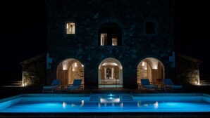 Vue nocturne d’un bâtiment doté d’une piscine, de trois portes en arc de cercle et de chaises longues.