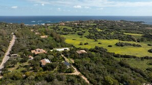 Vista aérea de una zona costera con casas dispersas, campos verdes y una carretera que lleva al mar.