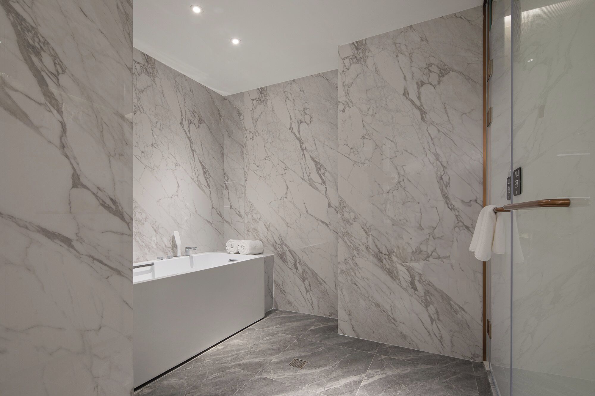 Een moderne badkamer met marmeren wanden, een glazen douchecabine en een ingebouwd wastafelmeubel.