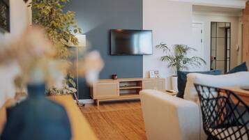 Una sala de estar moderna con una televisión de pantalla plana montada en la pared, un sofá, una mesa de centro y una planta en maceta.