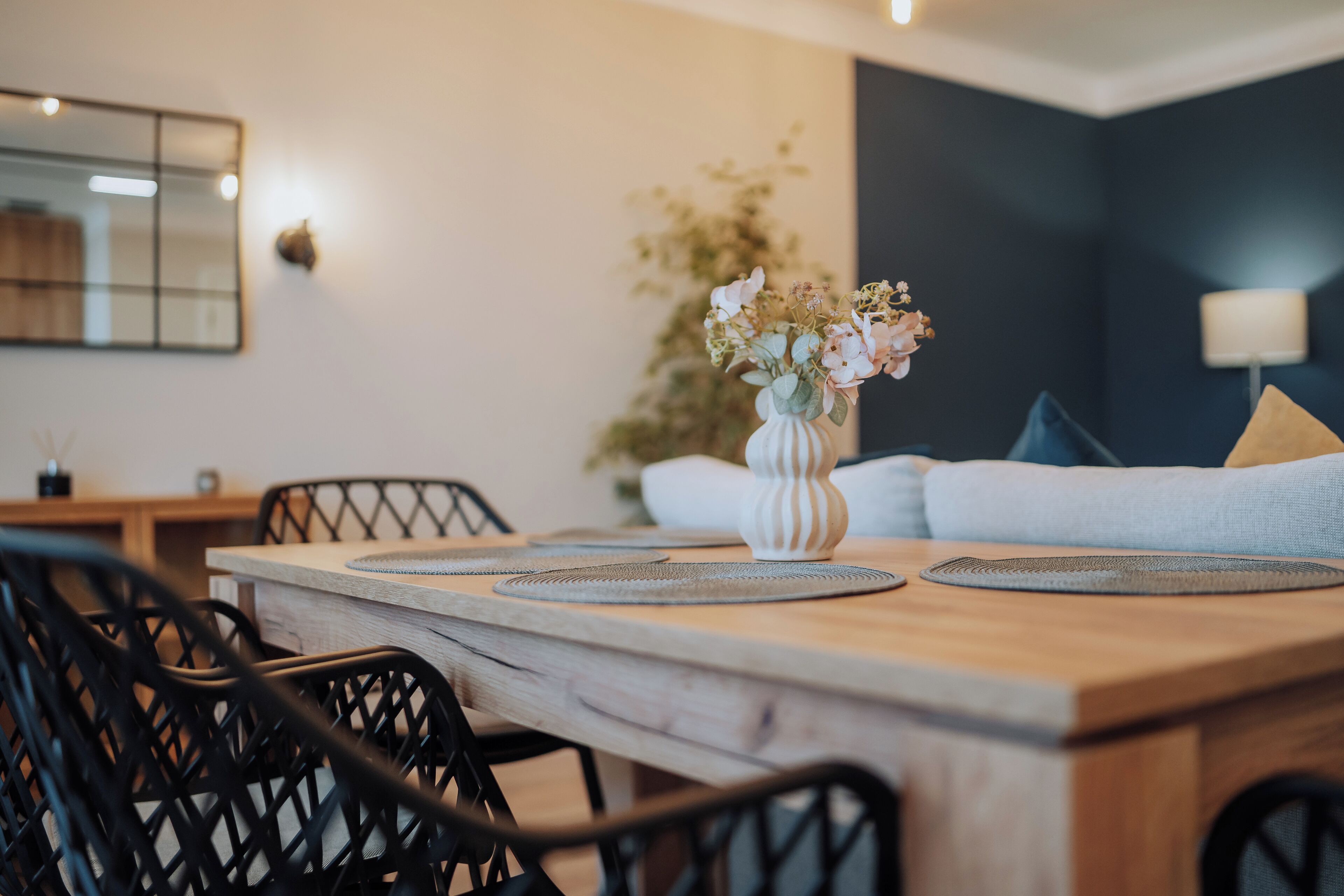 A dining area with a wooden table, black chairs, and a vase with flowers.