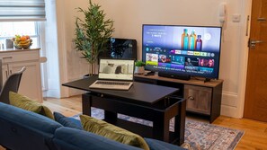 A modern living room with a laptop on a table, a television displaying a movie, a sofa, and a decorative plant. - 36 Queens Road Garden (Reading)