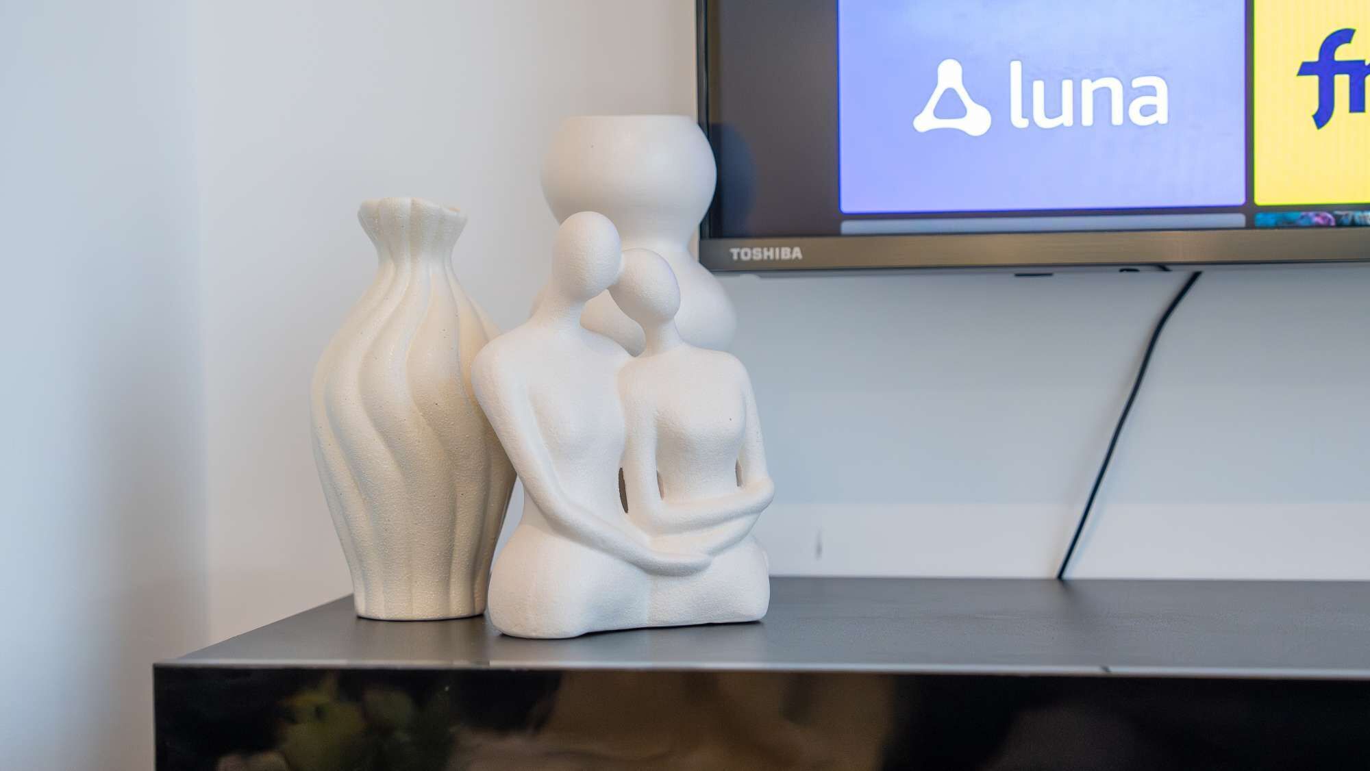 A flat-screen TV displaying the Luna logo, two white sculptures, and a Toshiba TV stand.