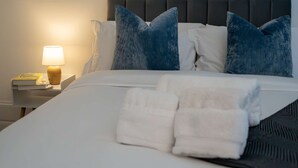 A neatly made bed with white linens and blue pillows, a bedside lamp, and a book on the nightstand. - 36 Queens Road Top Floor (Reading)