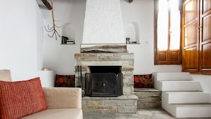 A living room with a stone fireplace, a beige sofa, and a staircase leading to an upper level. - Secluded Cottage Guesthouse in the Mountains (Volos)