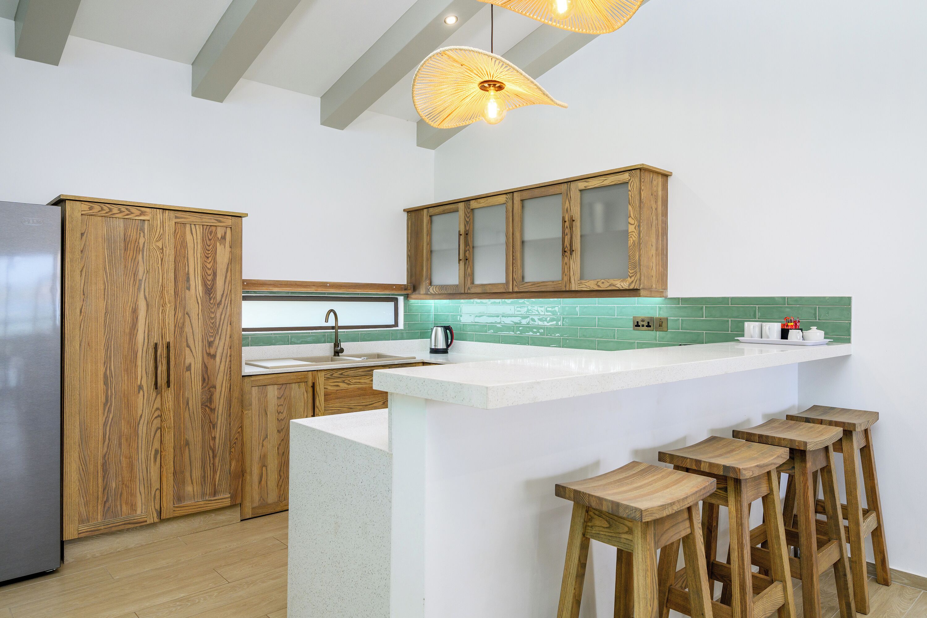 Eine moderne Küche mit Holzschränken, einem Edelstahlkühlschrank, einer Bar mit Hockern und einer grünen gefliesten Spritzschutzwand.