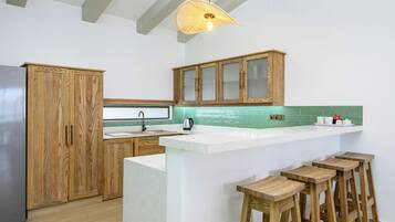Eine moderne Küche mit Holzschränken, einem Edelstahlkühlschrank, einer Bar mit Hockern und einer grünen gefliesten Spritzschutzwand.