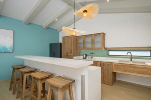A modern kitchen with a bar area, wooden stools, and a hanging light fixture. - San Martinho Vila Azul (Praia do Bilene)