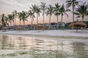 Ein Strandgrundstück mit strohgedeckten Gebäuden, Palmen und einem Sandstrand.
