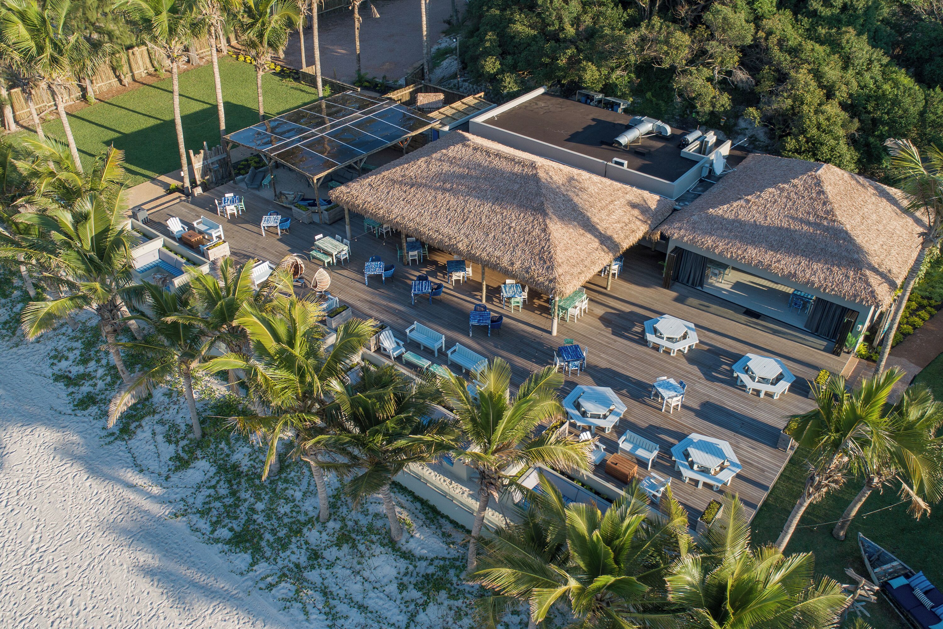 An aerial view of a resort with multiple thatched-roof structures, a pool area, and beach access.