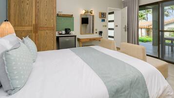 Habitación de hotel con cama, escritorio, espejo, kitchenette pequeño y puerta de vidrio corrediza a un balcón.