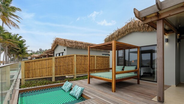 Una terraza de madera con piscina, una estructura de techo de paja y una barandilla de cristal.