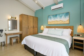 A bedroom with a bed, bedside tables, a wardrobe, a desk, and an air conditioning unit. - San Martinho Vila Azul (Praia do Bilene)