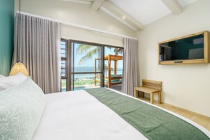 Una habitación de hotel con cama, televisor, sillón y vista al mar.
