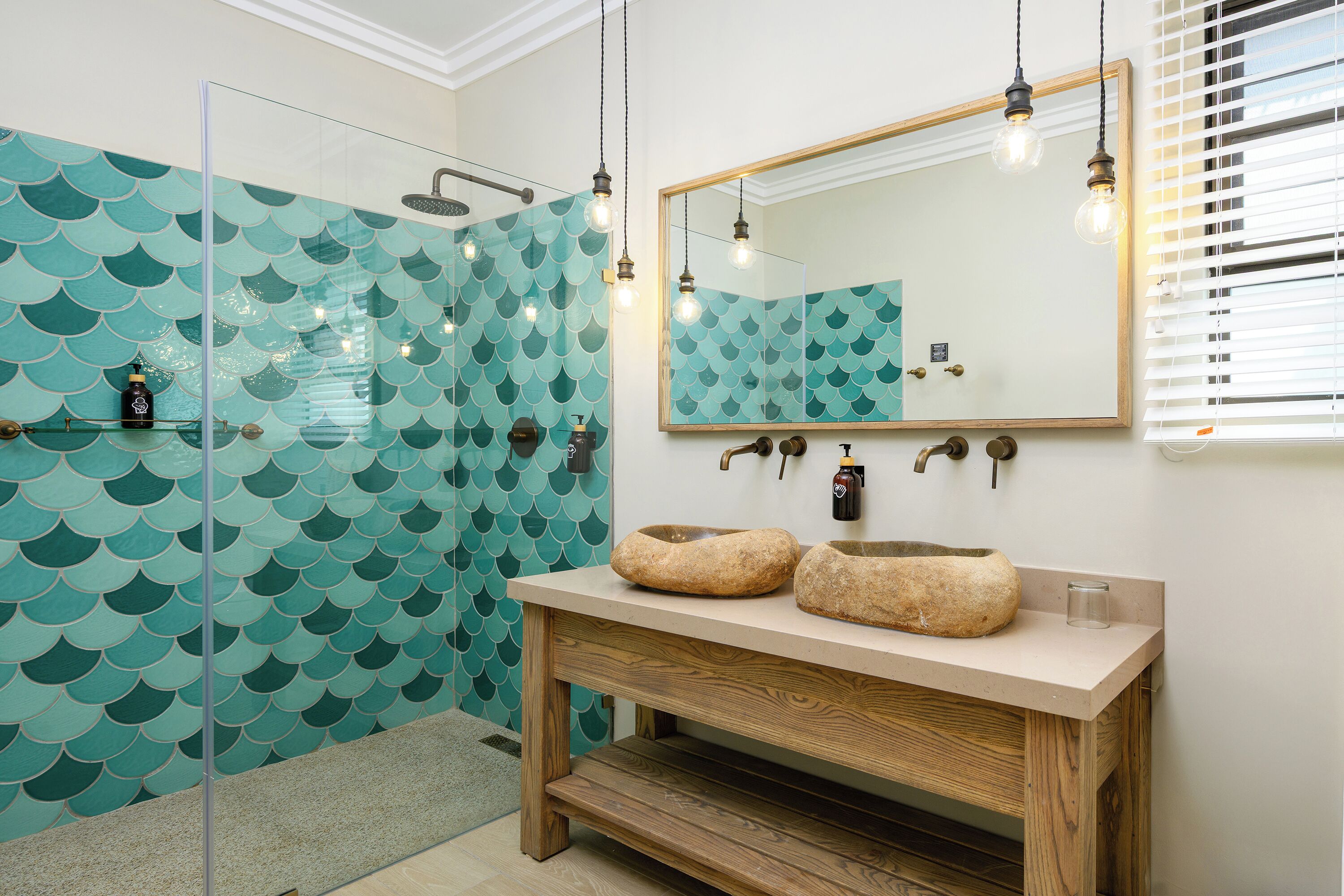 Une salle de bain dotée d’une douche à parois de verre, d’un meuble-lavabo en bois avec un vasque en pierre et d’un miroir encadré en bois.