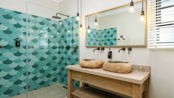Une salle de bain dotée d’une douche à parois de verre, d’un meuble-lavabo en bois avec un vasque en pierre et d’un miroir encadré en bois.