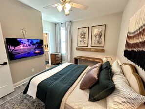 Un dormitorio con cama, televisión, ventilador de techo y obras de arte en las paredes.