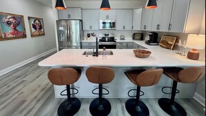 A modern kitchen with white cabinets, a central island with bar stools, stainless steel appliances, and pendant lighting.