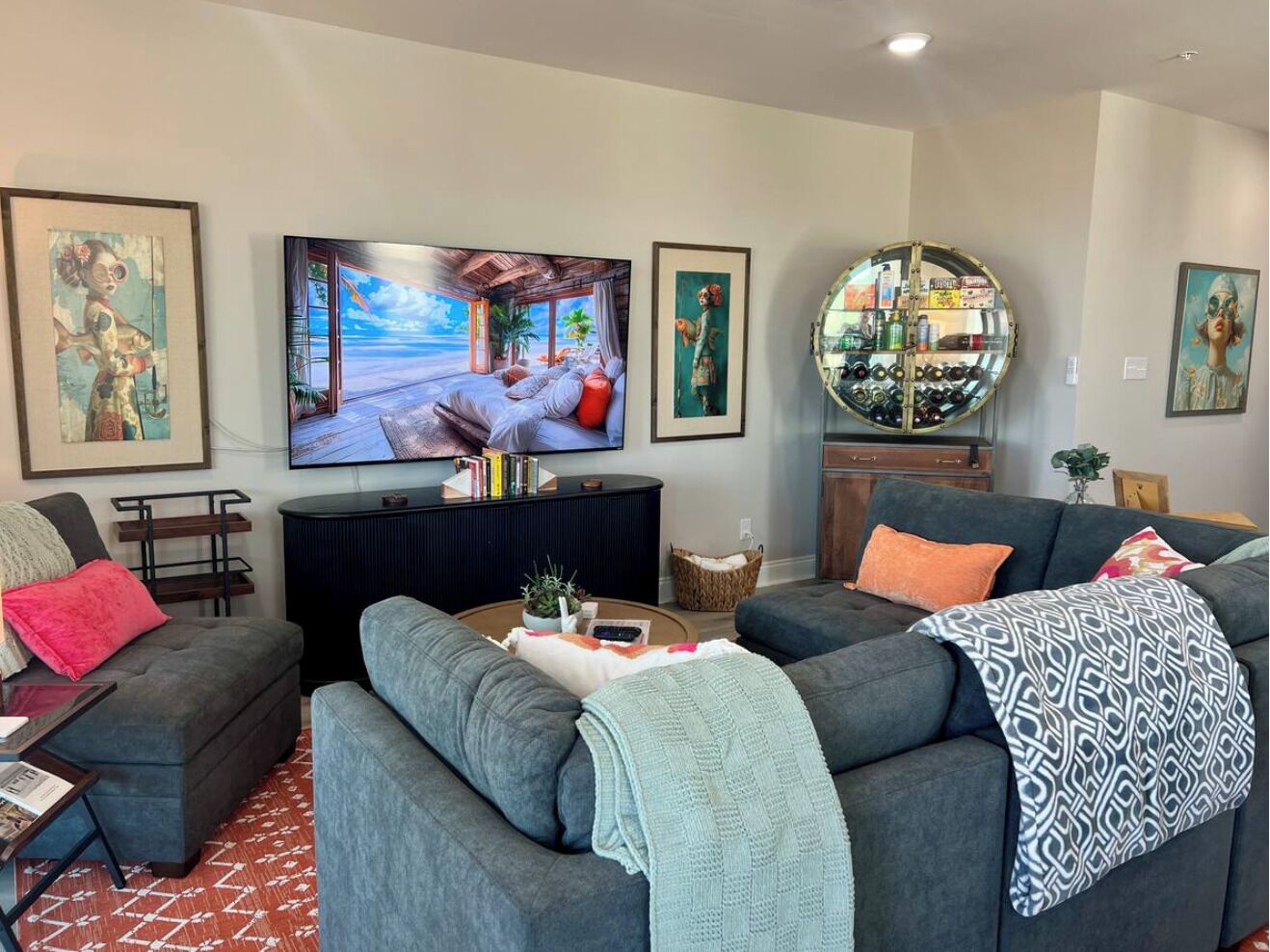 A living room with a large flat-screen TV, grey sofas, a coffee table, and framed artwork on the walls.